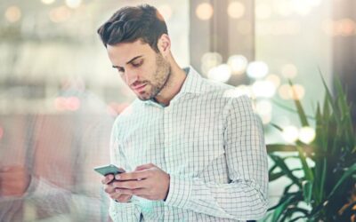 Homme d'affaires en chemise à carreaux consultant son PS3838 Mobile devant une fenêtre moderne.